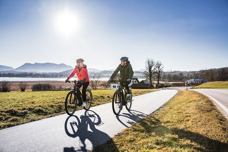 Zwei Personen fahren Fahrräder auf ländlichem Radweg bei Sonnenschein